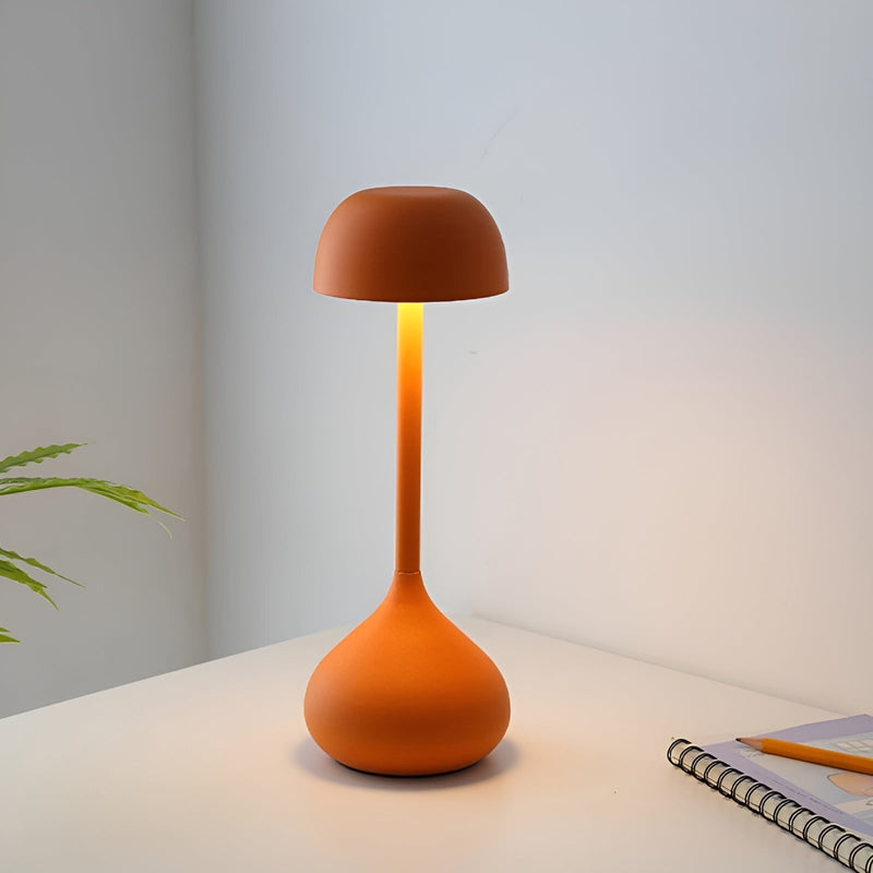 Orangefarbene Tischlampe aus Metall, modernes Design, auf weißem Tisch neben Notizbuch.