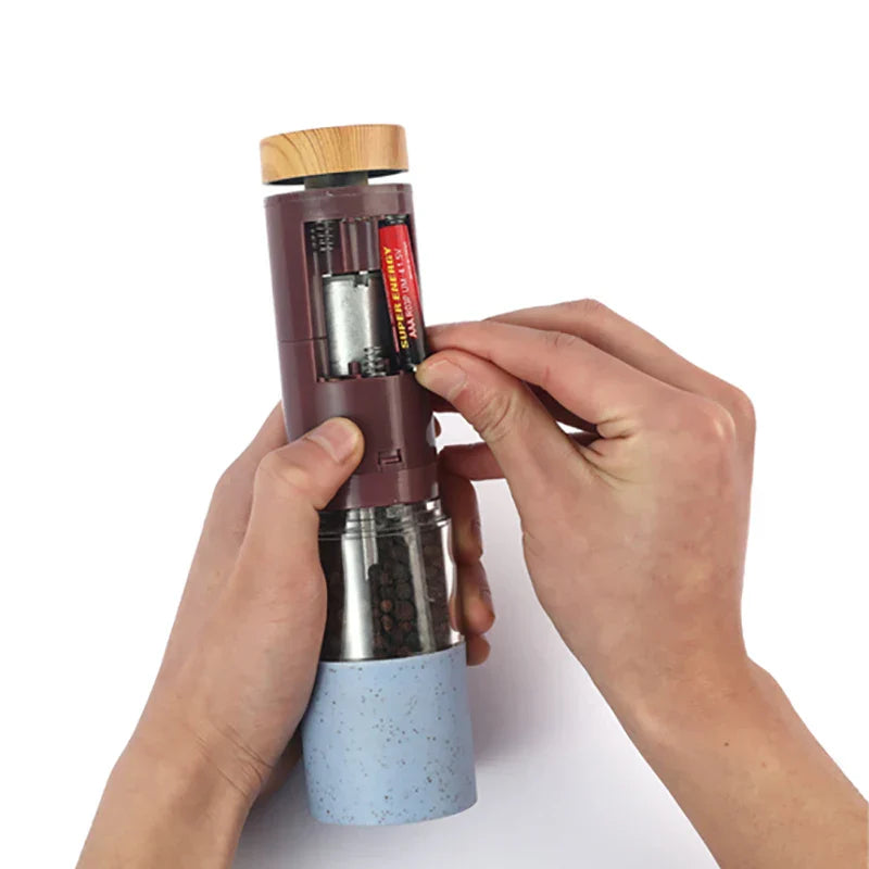 Elektrische Pfeffermühle mit Batteriefach, Holzdeckel, Edelstahl, blauem Griff, in Hand gehalten.