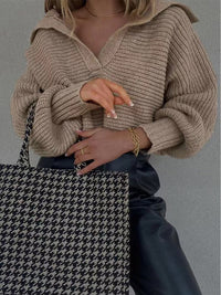 Frau mit beigem Strickpullover, Hahnentritt-Tasche und schwarzer Lederhose.