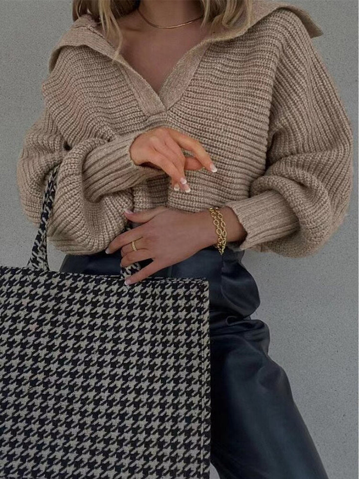 Frau mit beigem Strickpullover, Hahnentritt-Tasche und schwarzer Lederhose.
