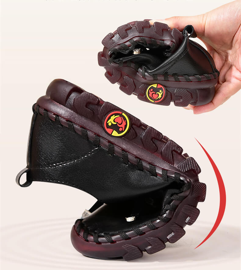 Schwarze, flexible Kinderschuhe mit rutschfester Sohle, handgehalten, rot-braune Details.