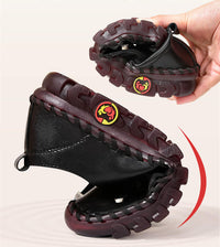 Schwarze, flexible Kinderschuhe mit rutschfester Sohle, handgehalten, rot-braune Details.