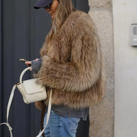 Frau mit brauner Kunstpelzjacke, blauer Jeans, weißer Tasche, Smartphone, draußen.