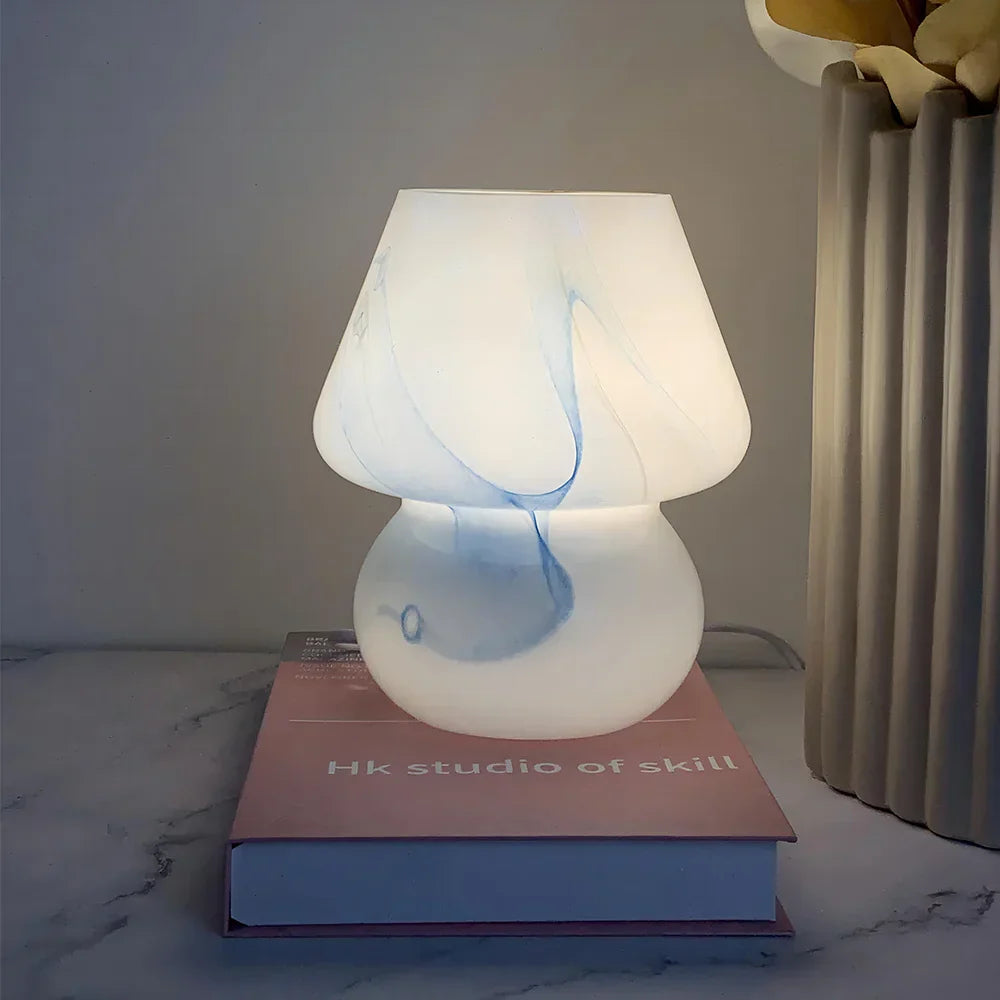 Weiße Tischlampe aus Glas mit blauen Akzenten auf rosa Buch, moderne Wohnkultur.
