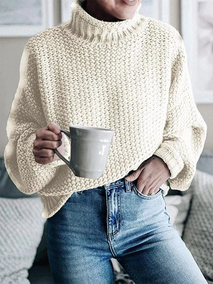 Frau in cremefarbenem Strickpullover hält graue Tasse, lässige Mode, gemütlicher Look.