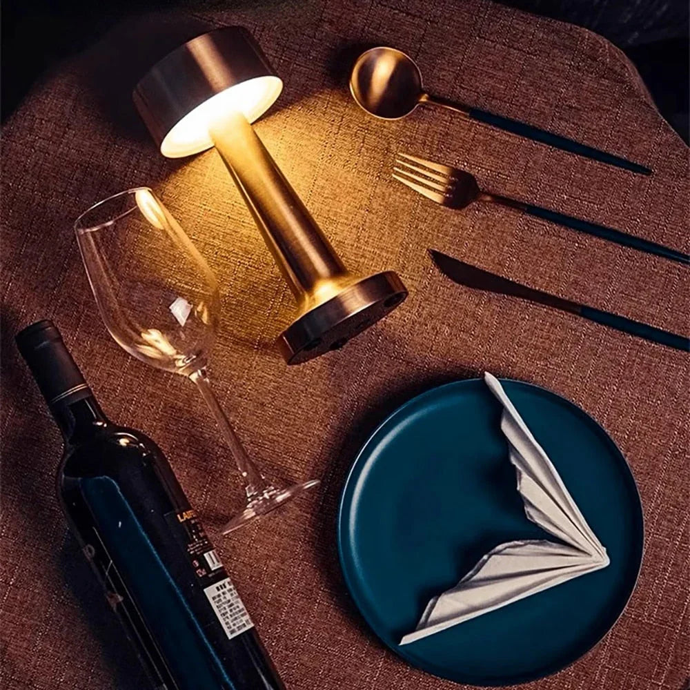 Elegante Tischdekoration mit Weinglas, Flasche, Teller, Besteck und goldener Tischlampe.