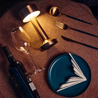 Elegante Tischdekoration mit Weinglas, Flasche, Teller, Besteck und goldener Tischlampe.