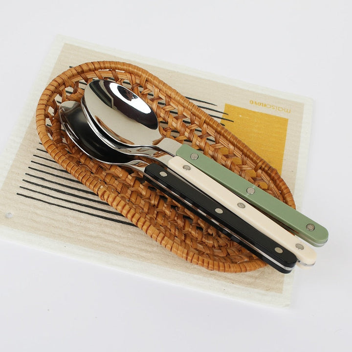 Löffelset mit bunten Griffen auf geflochtenem Tablett, Edelstahl, modern, stilvoll.