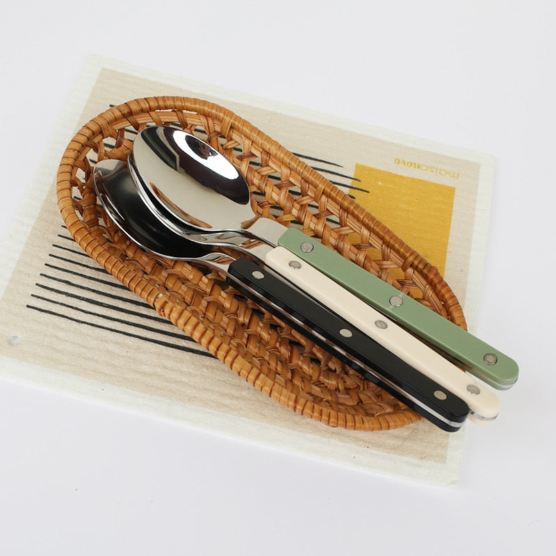 Löffelset mit bunten Griffen auf geflochtenem Tablett, Edelstahl, modern, stilvoll.