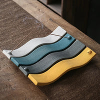 Bunte Keramik-Räucherstäbchenhalter in Wellenform auf Holztisch.