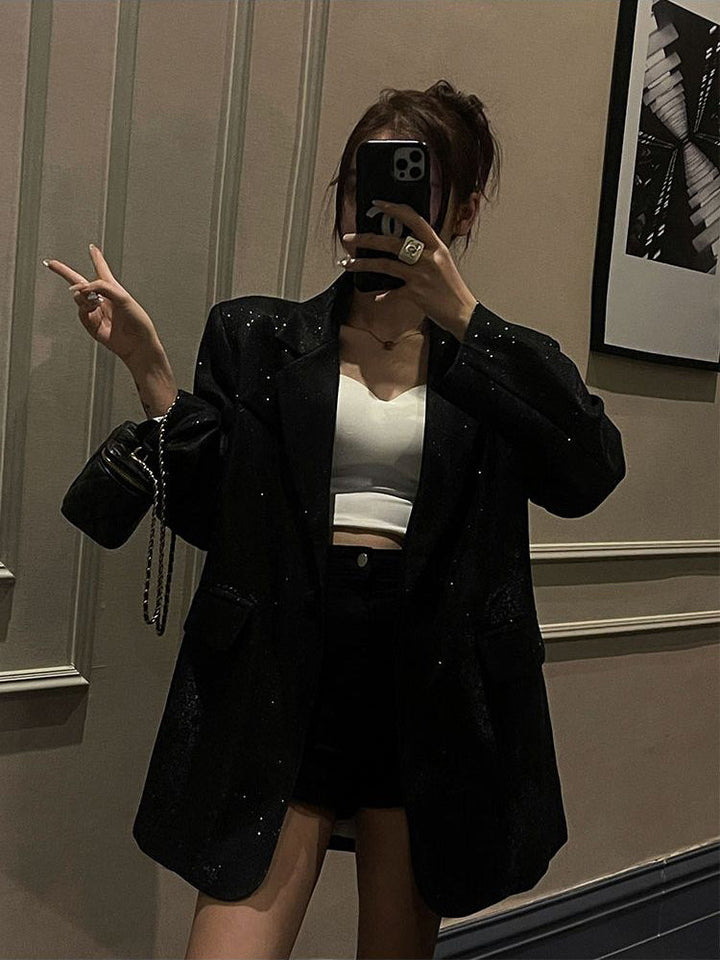 Frau in schwarzem Glitzerblazer, weißem Top, schwarzer Tasche, macht ein Selfie.