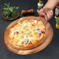 Hand hält Holzbrett mit tropischer Pizza, Ananas, Drachenfrucht, auf dunklem Tisch.