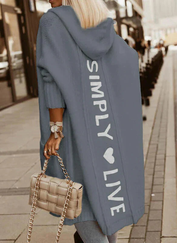 Frau in blauem Kapuzenmantel mit "Simply Live"-Aufdruck, beige gesteppte Handtasche.