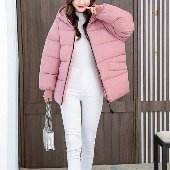 Frau in rosa Daunenjacke, weiße Hose, silberne Handtasche, Wintermode, stilvoll, warm.