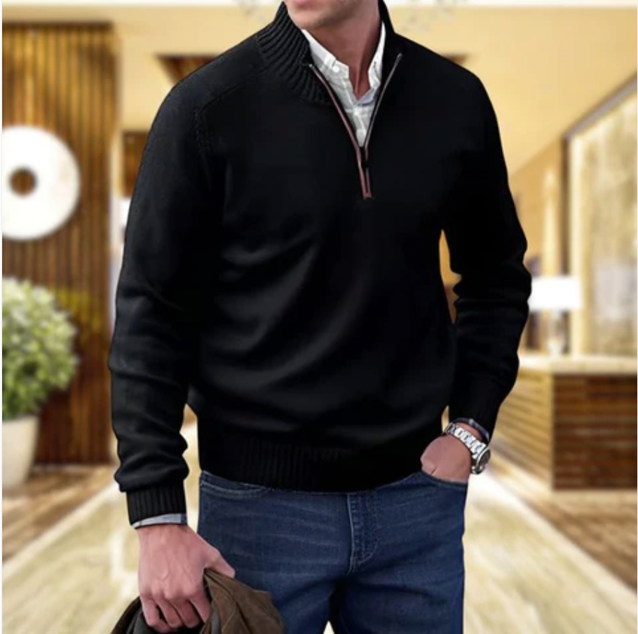 Mann in schwarzem Pullover mit Reißverschluss, blaue Jeans, moderne Innenraumkulisse.