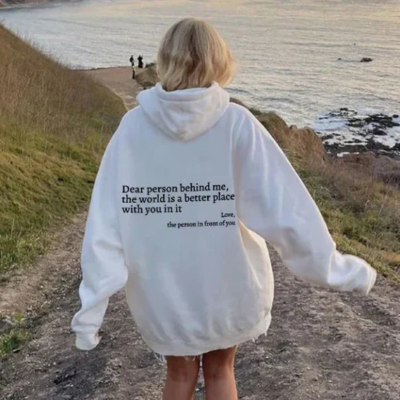 Weiße Oversize-Hoodie mit schwarzem Text, Frau am Küstenweg, lässige Mode, Naturkulisse.