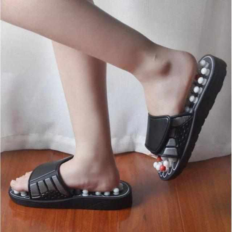 Schwarze Akupressur-Sandalen mit Massagekugeln, Fußreflexzonenmassage, Holzfußboden.