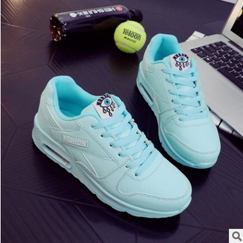Hellblaue Sneaker mit Augenmotiv, Tennisschläger und Ball auf schwarzem Tisch.