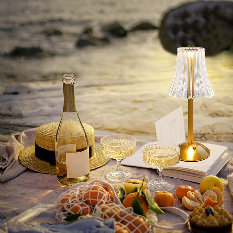 Strandpicknick mit Weinflasche, Gläsern, Obst und Tischlampe bei Sonnenuntergang.