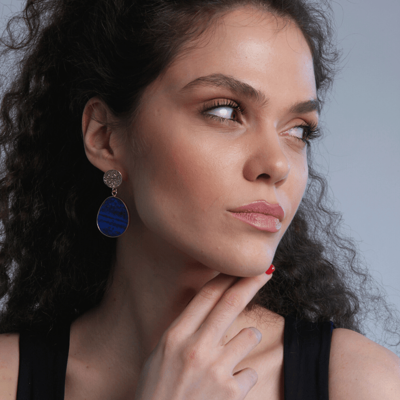 Frau mit blauen Ohrringen, lockigem Haar, schwarzem Top, nachdenklicher Blick.
