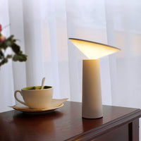 Moderne LED-Tischlampe, weiß, konisch, auf Holztisch neben Kaffeetasse, Innenbeleuchtung.