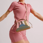 Frau in rosa Kleid mit bunter Designer-Handtasche, geometrisches Muster, Schulterriemen.