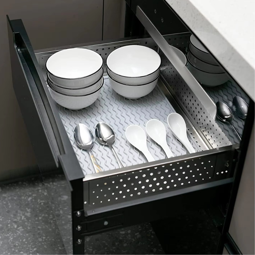 Offene Küchenschublade mit weißen Schalen und Löffeln auf rutschfester Matte.