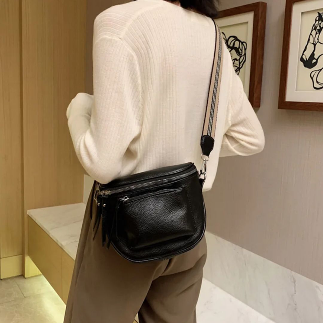 Frau mit schwarzer Leder-Umhängetasche, cremefarbenem Pullover, brauner Hose im modernen Raum.