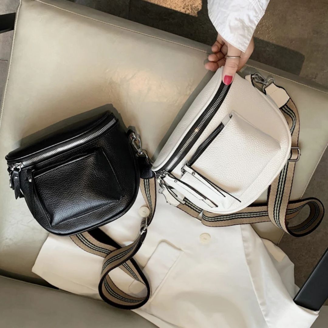Schwarze und weiße Leder-Umhängetaschen mit Reißverschluss auf beigem Stuhl.