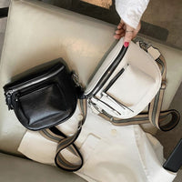 Schwarze und weiße Leder-Umhängetaschen mit Reißverschluss auf beigem Stuhl.