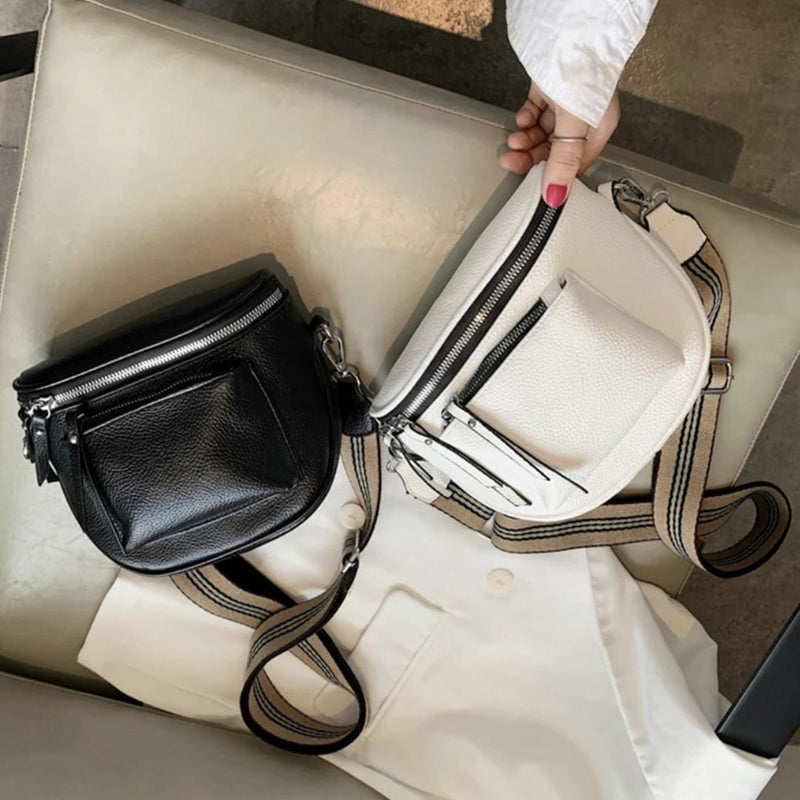 Schwarze und weiße Leder-Umhängetaschen mit Reißverschluss auf beigem Stuhl.