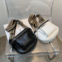 Schwarze und weiße Leder-Umhängetaschen mit gestreiften Riemen auf transparentem Stuhl.