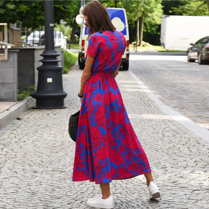 Frau im roten und blauen Blumenkleid auf Kopfsteinpflasterstraße, Sommermode, Rückansicht.