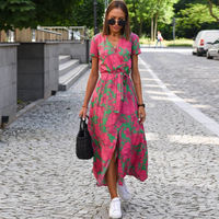 Frau im pink-grünen Sommerkleid mit Blumenmuster, trägt schwarze Tasche, weiße Sneaker.