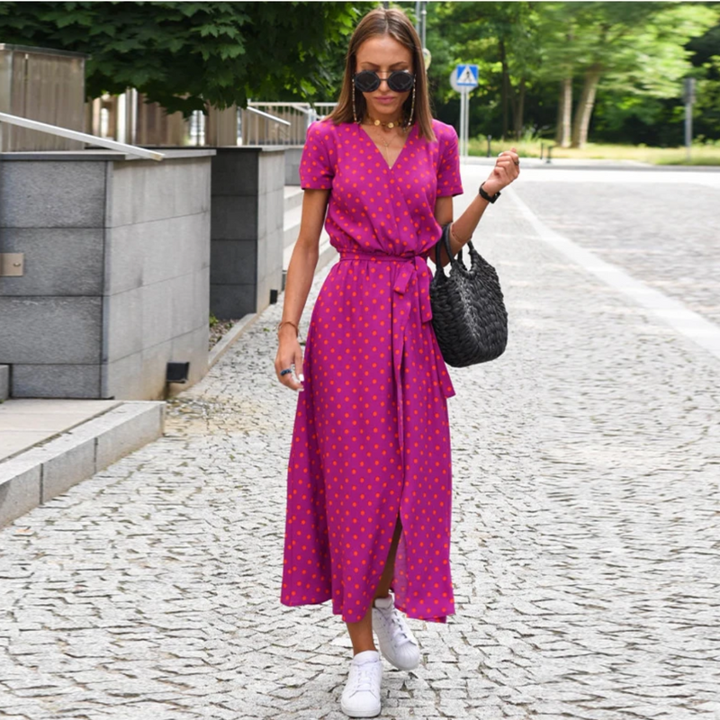 Frau in pinkem gepunktetem Kleid, Sonnenbrille, weiße Sneaker, schwarze Tasche, Sommermode.