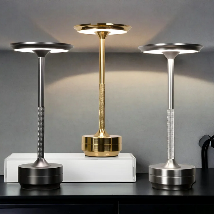 Drei moderne LED-Tischlampen in Gold, Silber und Schwarz auf weißem Regal, stilvolles Design.