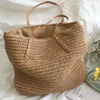 Große beige Strohtasche mit Ledergriffen auf weißem Hintergrund, ideal für Strand oder Einkauf.