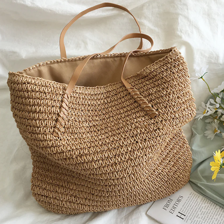 Große beige Strohtasche mit Ledergriffen auf weißem Hintergrund, ideal für Strand oder Einkauf.