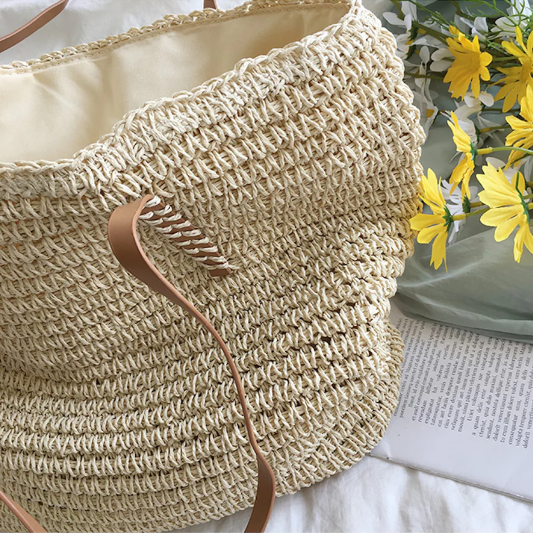 Geflochtener Strohtasche mit Lederriemen, beige, neben gelben Blumen, Sommermode Accessoire.
