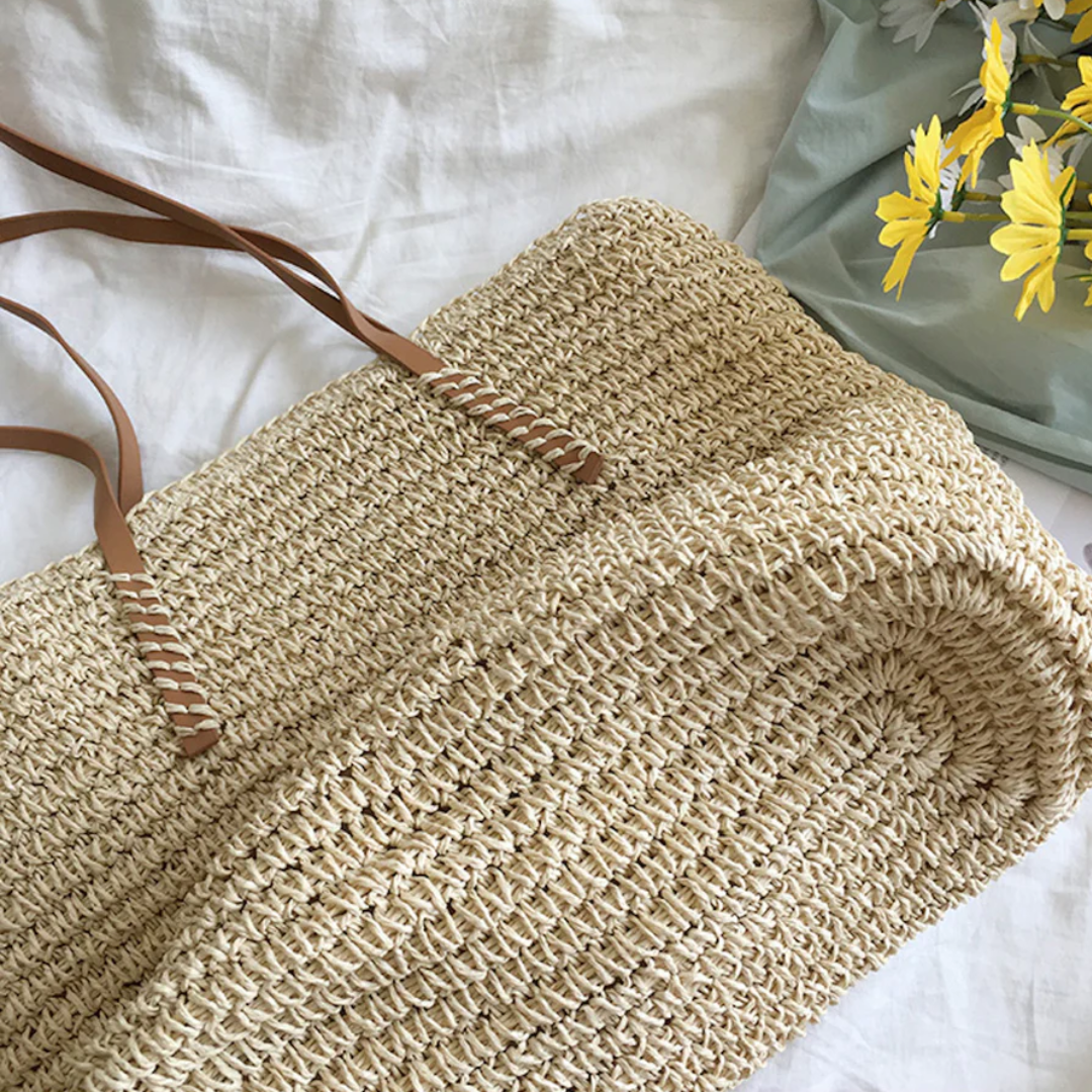 Geflochtener Strohtasche mit braunen Ledergriffen auf weißem Hintergrund, Sommermode Accessoire.