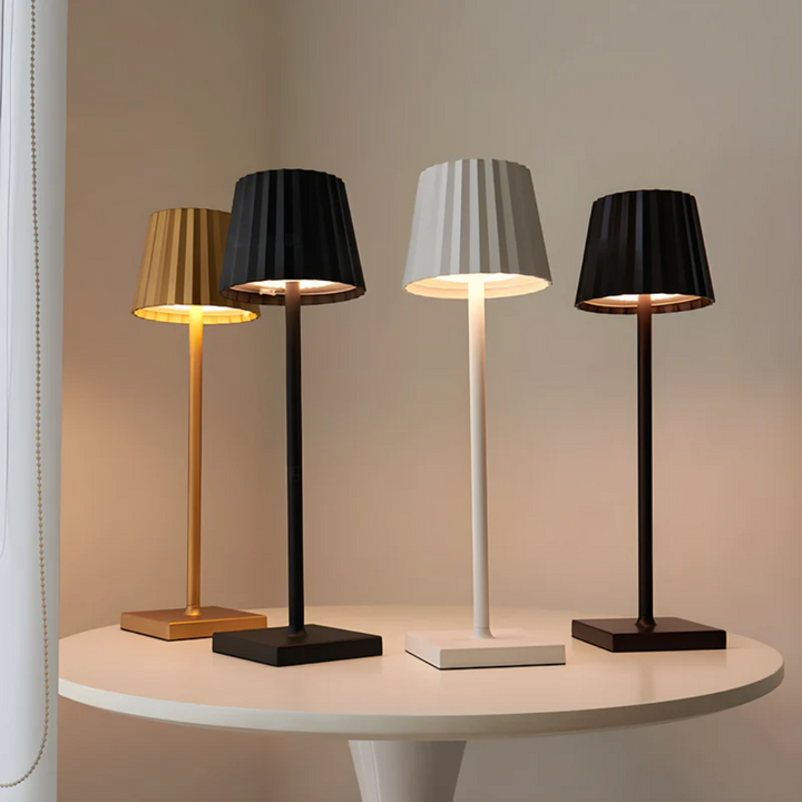 Vier moderne Tischlampen in Gold, Schwarz, Weiß und Braun auf rundem Tisch, minimalistisches Design.