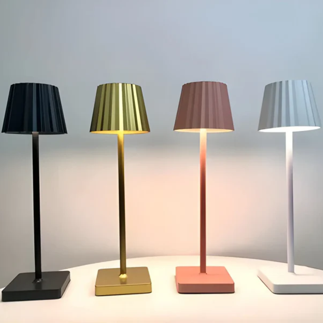 Vier moderne Tischlampen in Schwarz, Gold, Rosa und Weiß auf einem Tisch, minimalistisches Design.