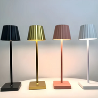 Vier moderne Tischlampen in Schwarz, Gold, Rosa und Weiß auf einem Tisch, minimalistisches Design.