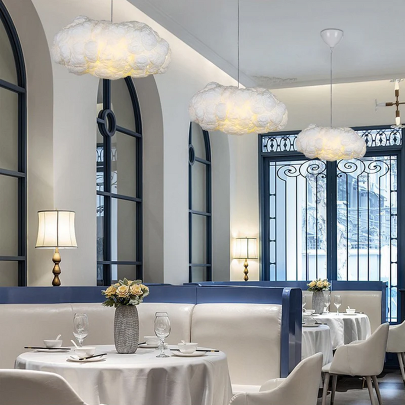 Wolkenförmige Pendelleuchte im modernen Restaurant, weiße Sofas, elegante Tischdekoration.