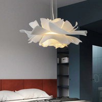 Moderne weiße Pendelleuchte in Blütenform über einem Bett in einem stilvollen Schlafzimmer.