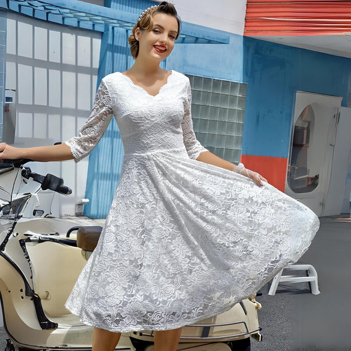 Frau in weißem Spitzenkleid vor Retro-Roller, lächelnd, urbaner Hintergrund.