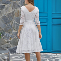 Frau in weißem Spitzenkleid mit Dreiviertelärmeln vor blauer Tür und Steinwand.