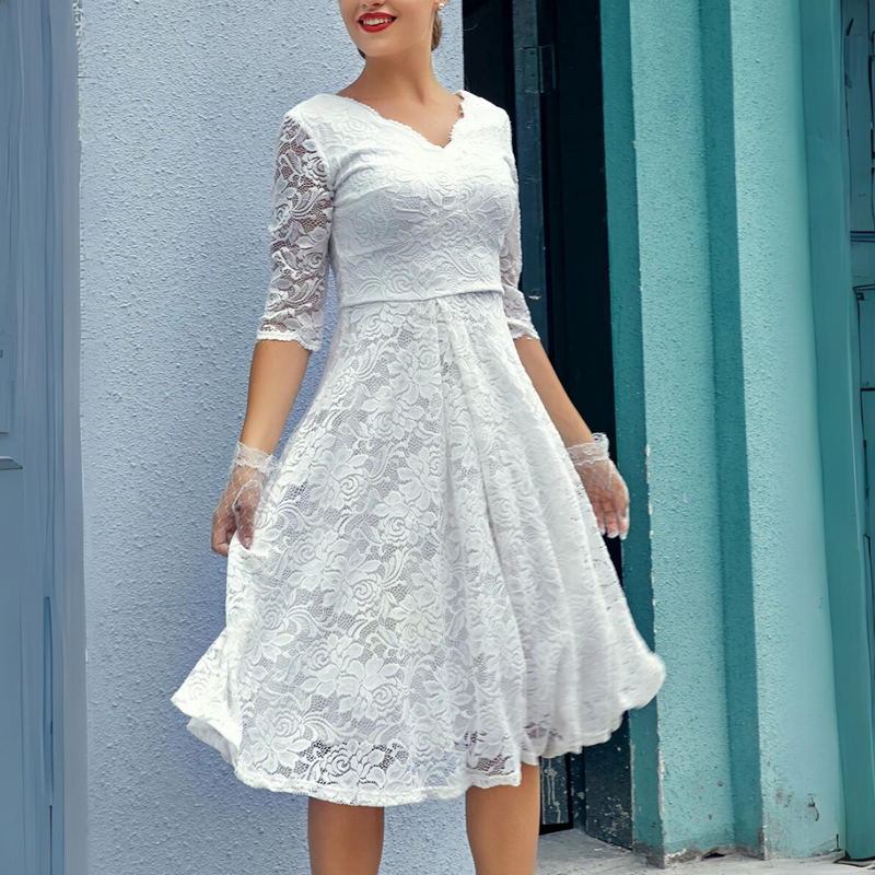 Frau in weißem Spitzenkleid mit Dreiviertelärmeln vor blauer Wand.