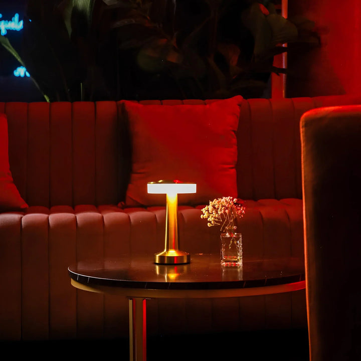 Goldene Tischlampe auf schwarzem Tisch, rotes Sofa im Hintergrund, moderne Wohnzimmerdekoration.