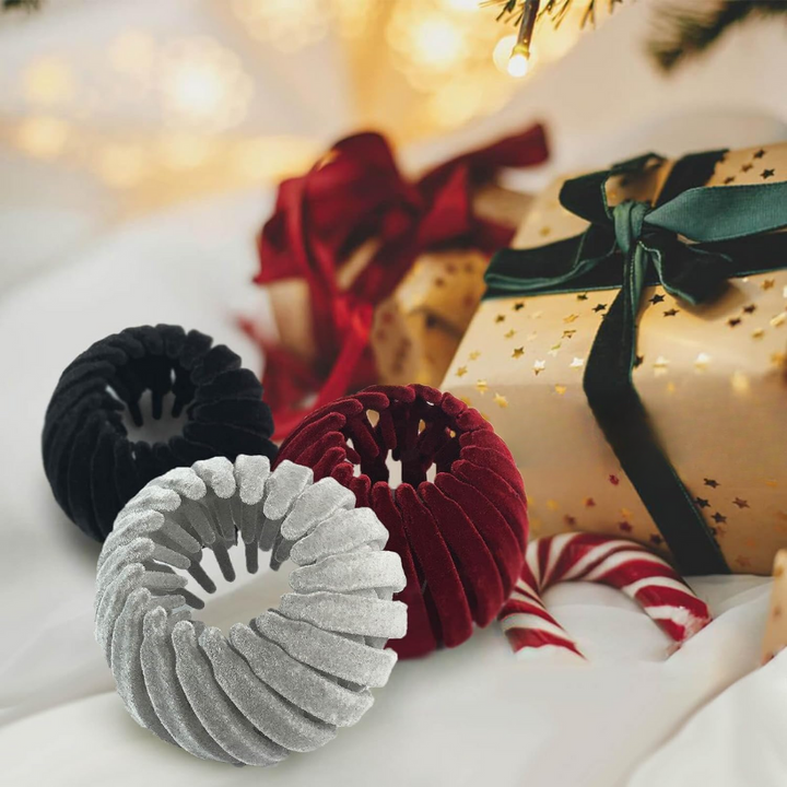 Drei Samt-Haargummis in Schwarz, Rot und Silber vor Weihnachtsgeschenk und Zuckerstange.